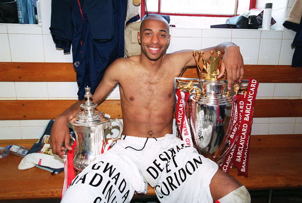 Arsenal legend Thierry Henry poses with FA Cup and Premier League trophies